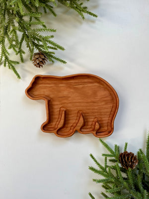 Wooden tray carved in the shape of a bear surrounded by pine branches and pine cones on white surface
