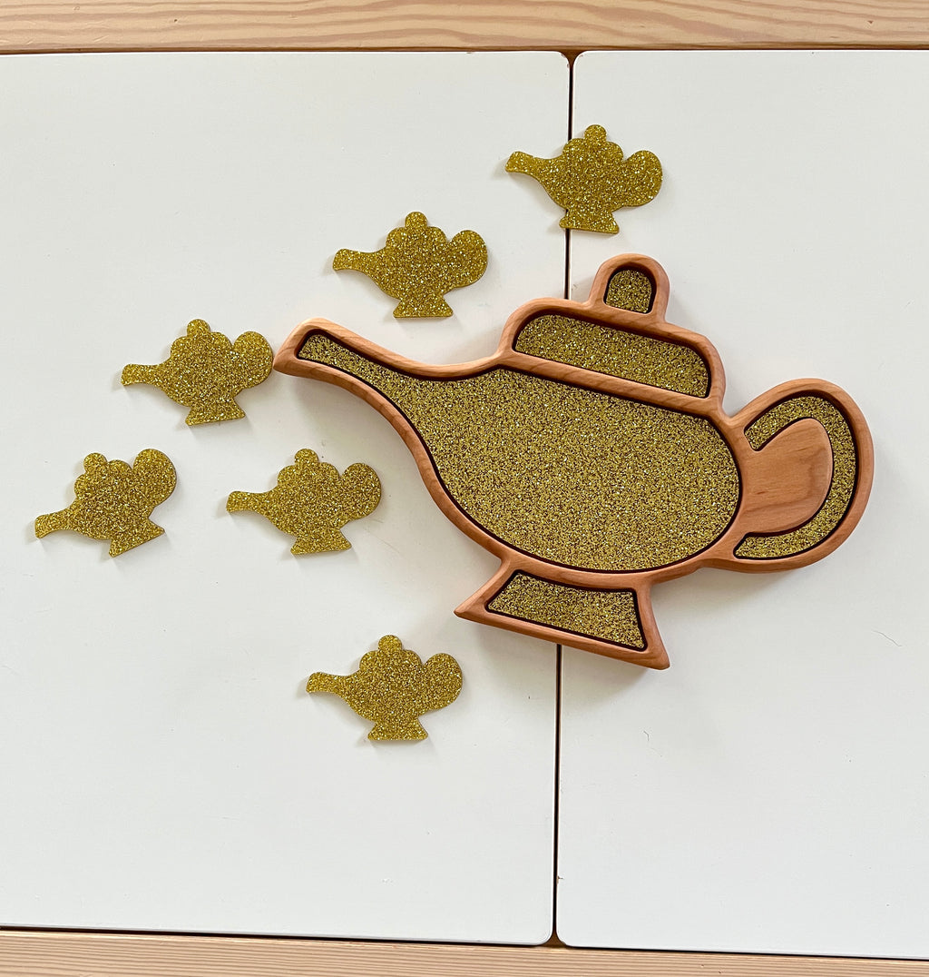Wooden tray shaped like a genie lamp filled with glittery gold material and glitter lamp cutouts on white surface