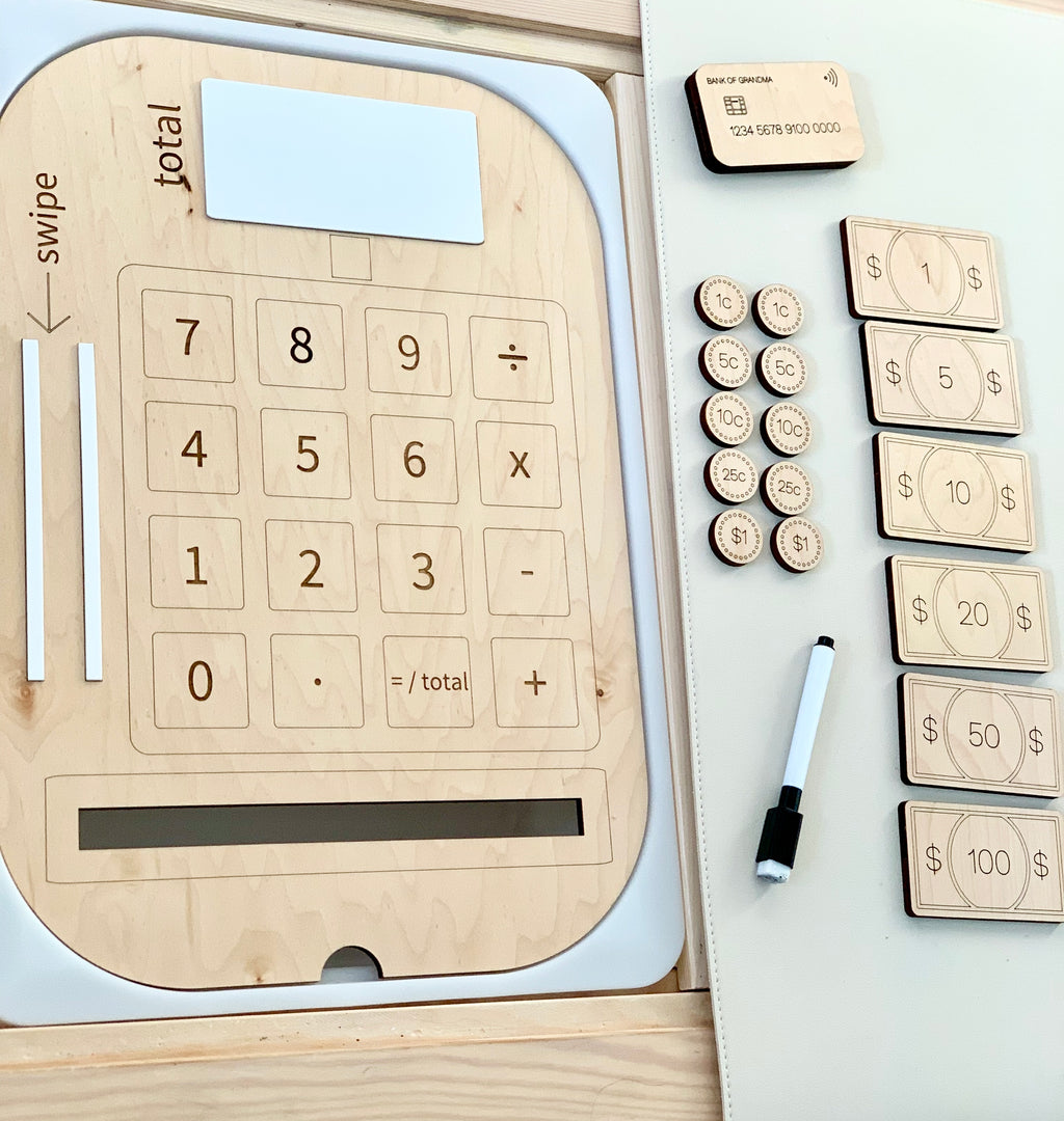 Wooden cash register insert with dry erase total, wooden credit card, play money bills and coins, and marker on white surface