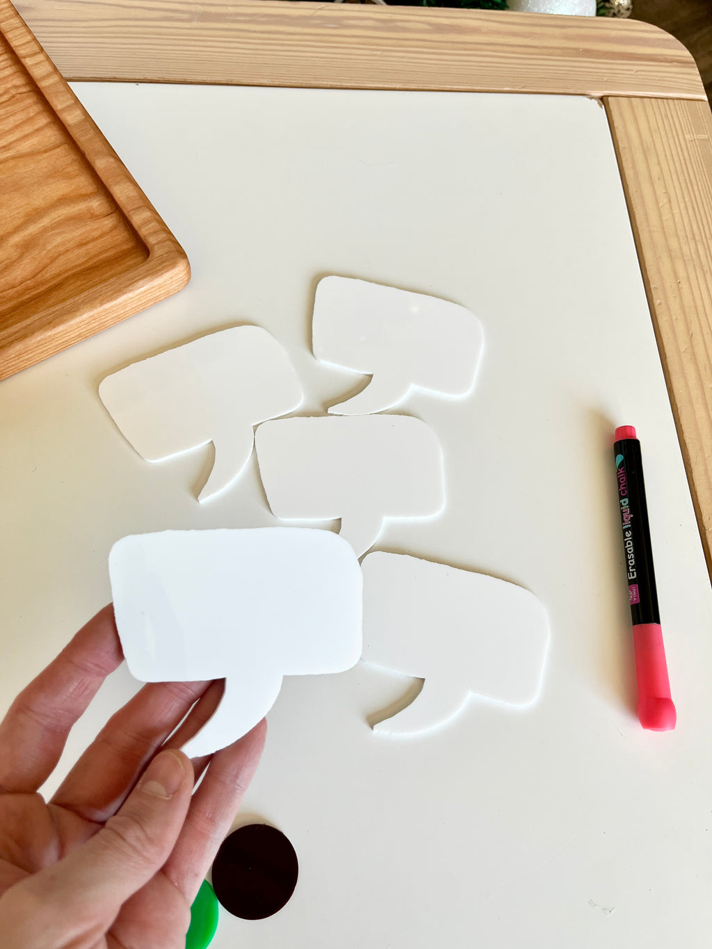Hand holding blank white speech bubble cutout with four similar cutouts and a pink marker on white table