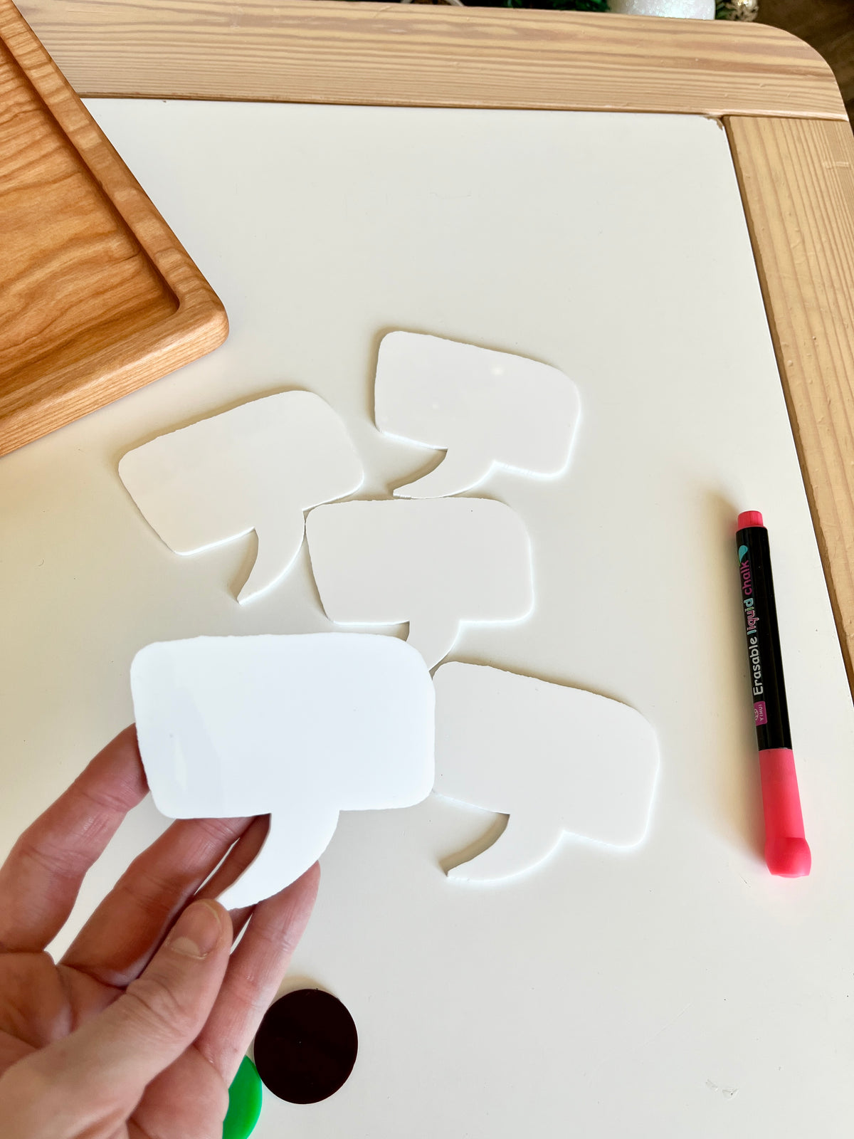 Hand holding blank white speech bubble cutout with four similar cutouts and a pink marker on white table