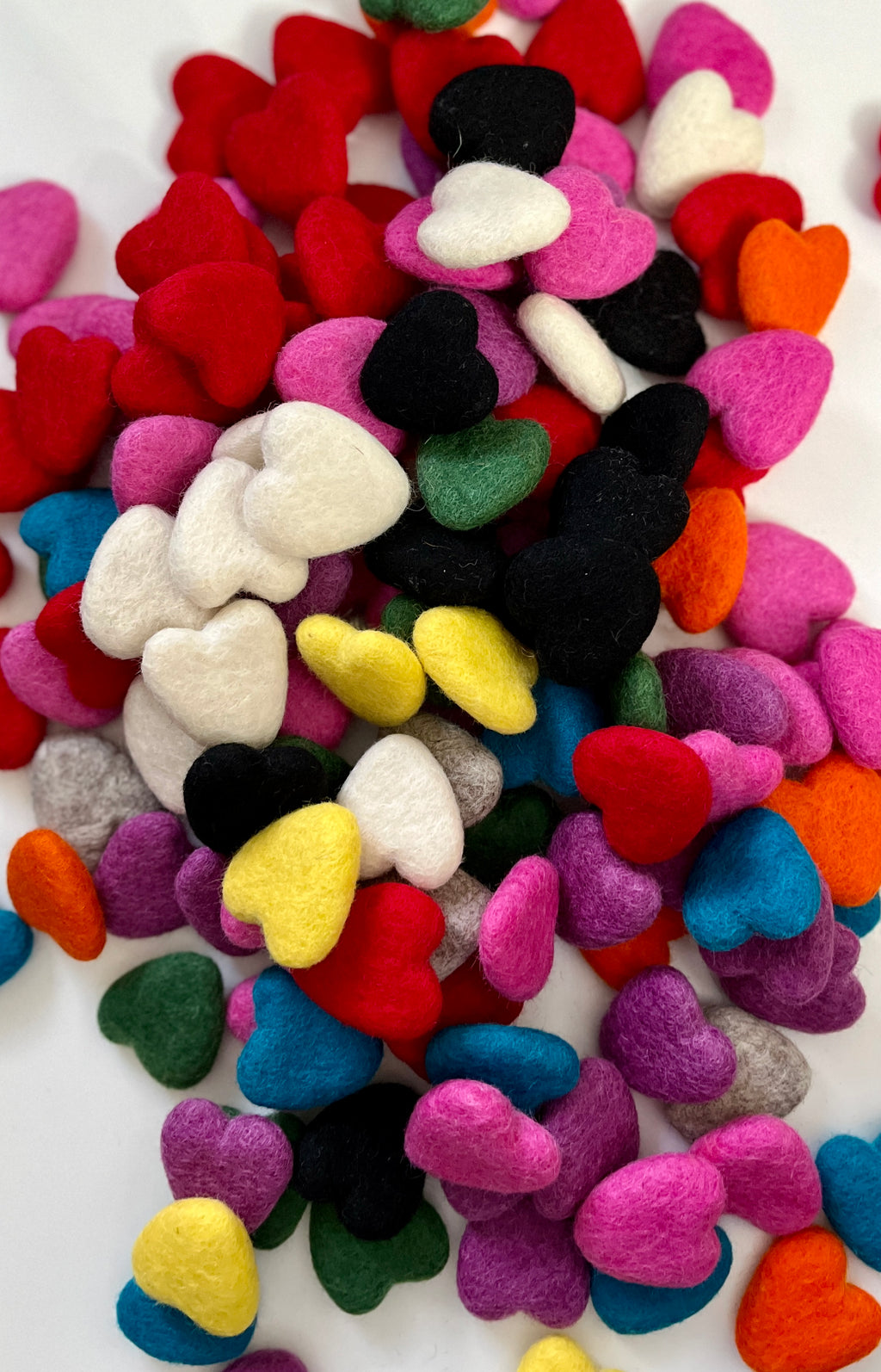 Assorted small felt hearts in various colors scattered on a white background in a close-up view