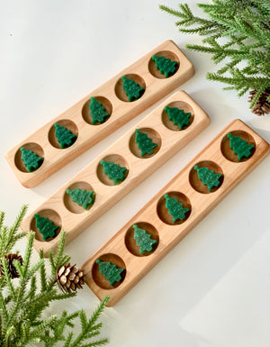 Three wooden five frame sensory trays with green tree-shaped counting gems on white surface with pine branches and pinecones