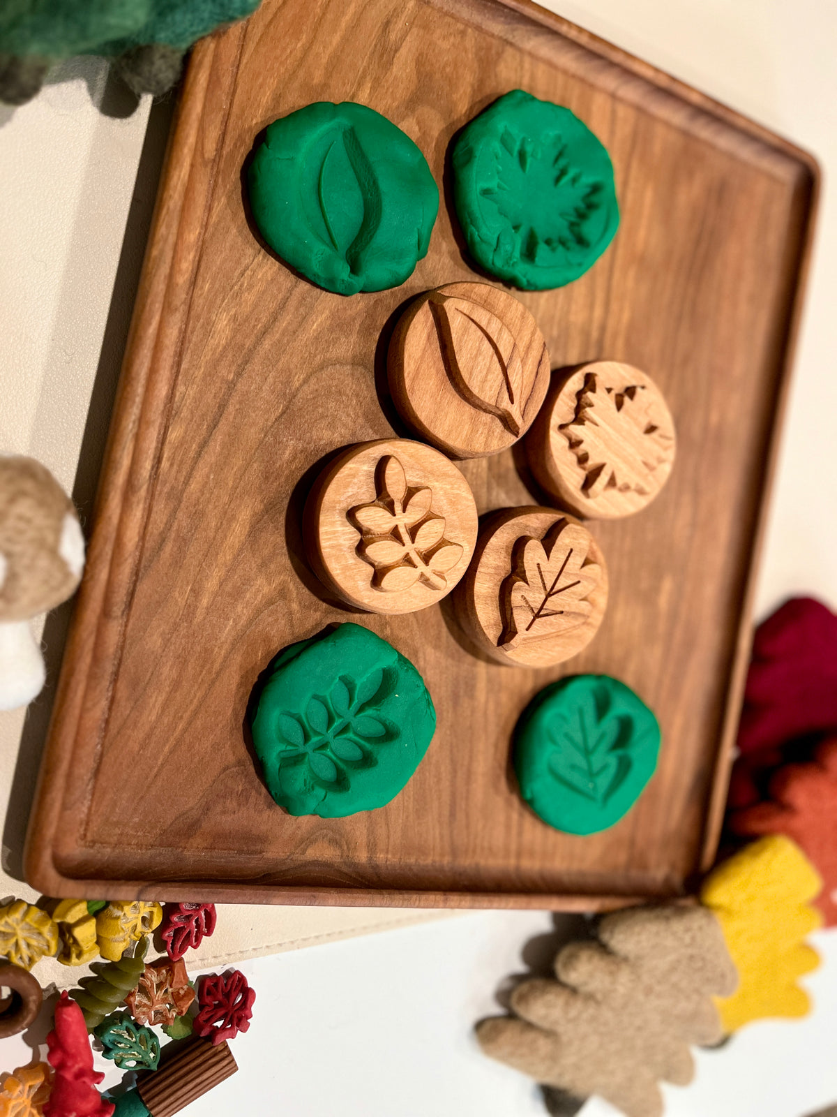 Wooden leaf imprint stamps with green playdough impressions displayed on a wooden tray surrounded by fall decor