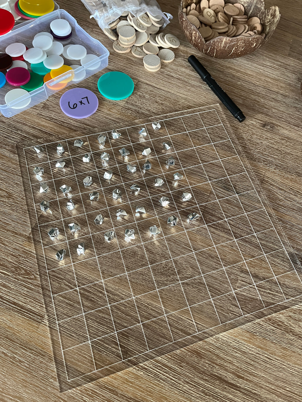 Dry Erasable Blank Open Ended 100 Frame Hundred Board on wood surface with clear grid and small white counters, black dry erase marker, colorful tokens in container, and wooden number discs, handcrafted homeschool education resources.