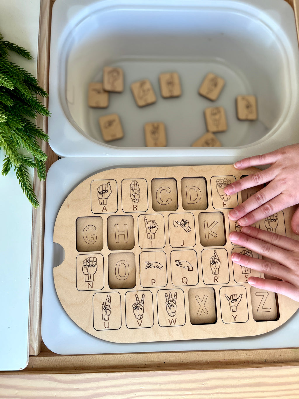 Small maple plywood ASL alphabet puzzle insert for Flisat bin with scattered wooden letter pieces and child’s hands