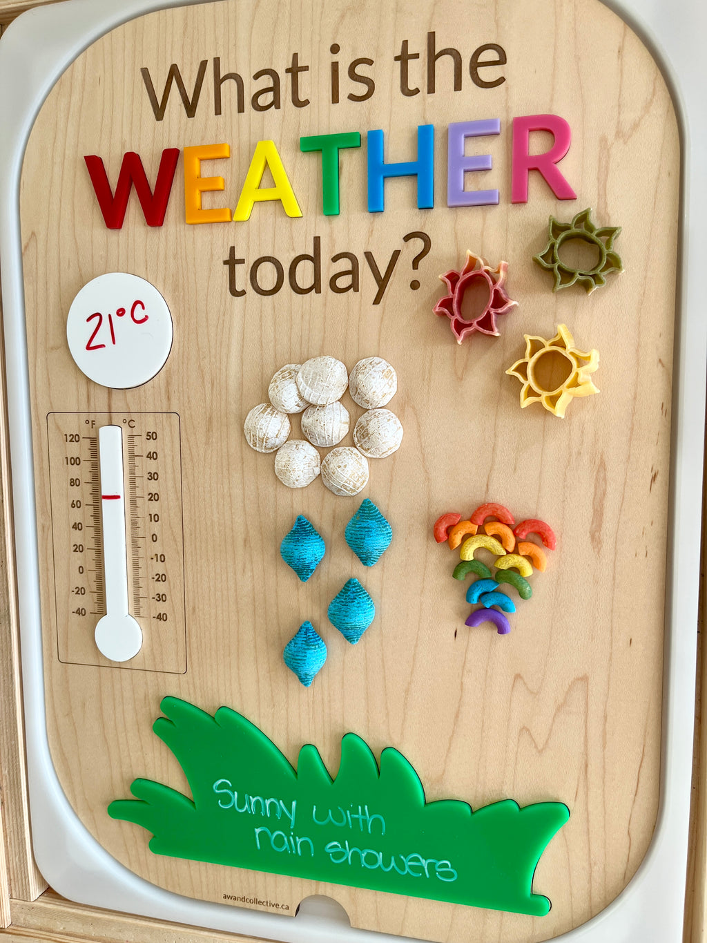 Wooden weather board with colorful letters, pasta shapes representing sun, clouds, rain, rainbow, and a thermometer showing 21°C