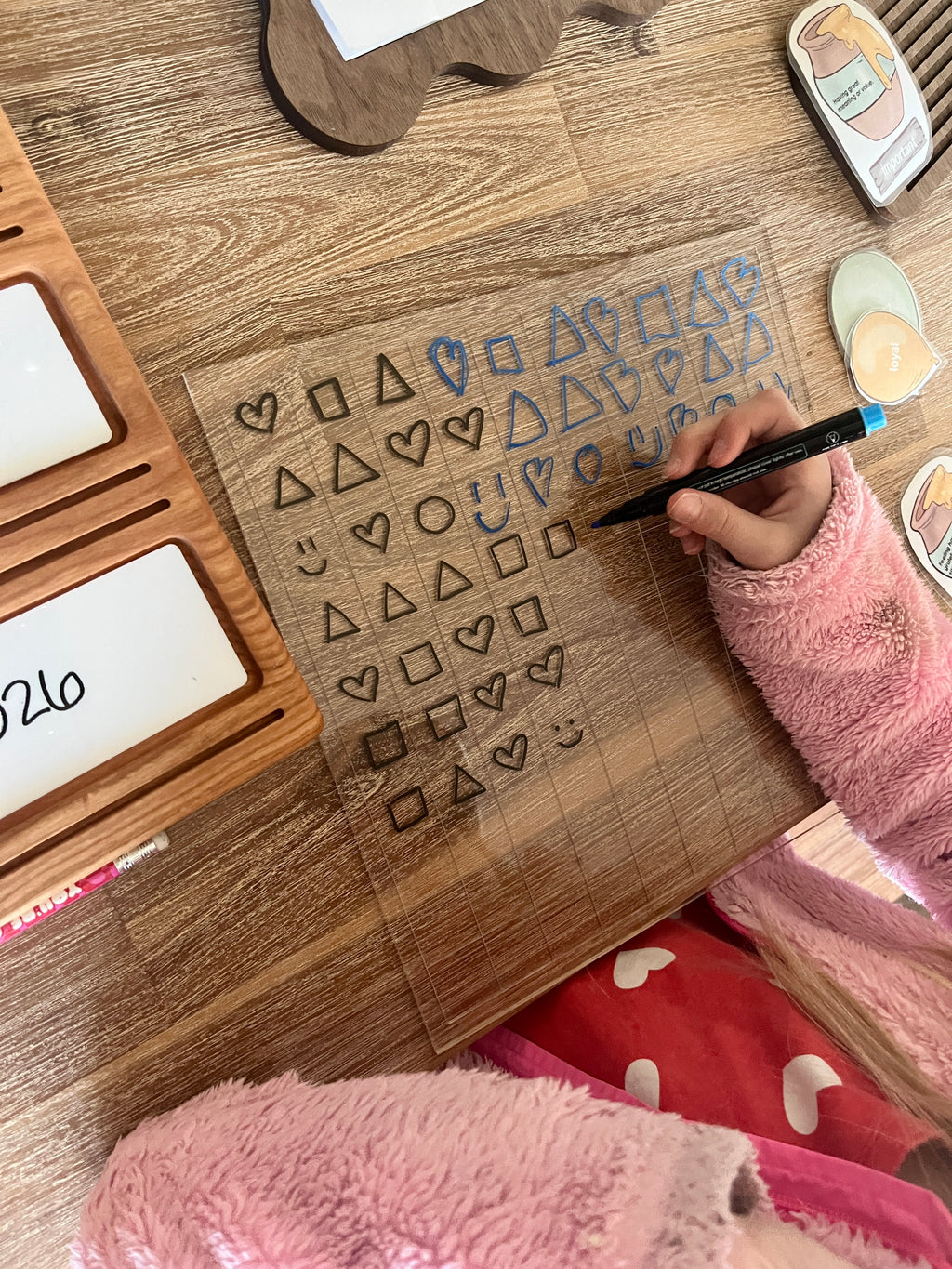 Dry Erasable Blank Open Ended 100 Frame Hundred Board on wood table with clear grid, child’s hand drawing shapes and symbols using black dry erase marker, handcrafted homeschool education resources.