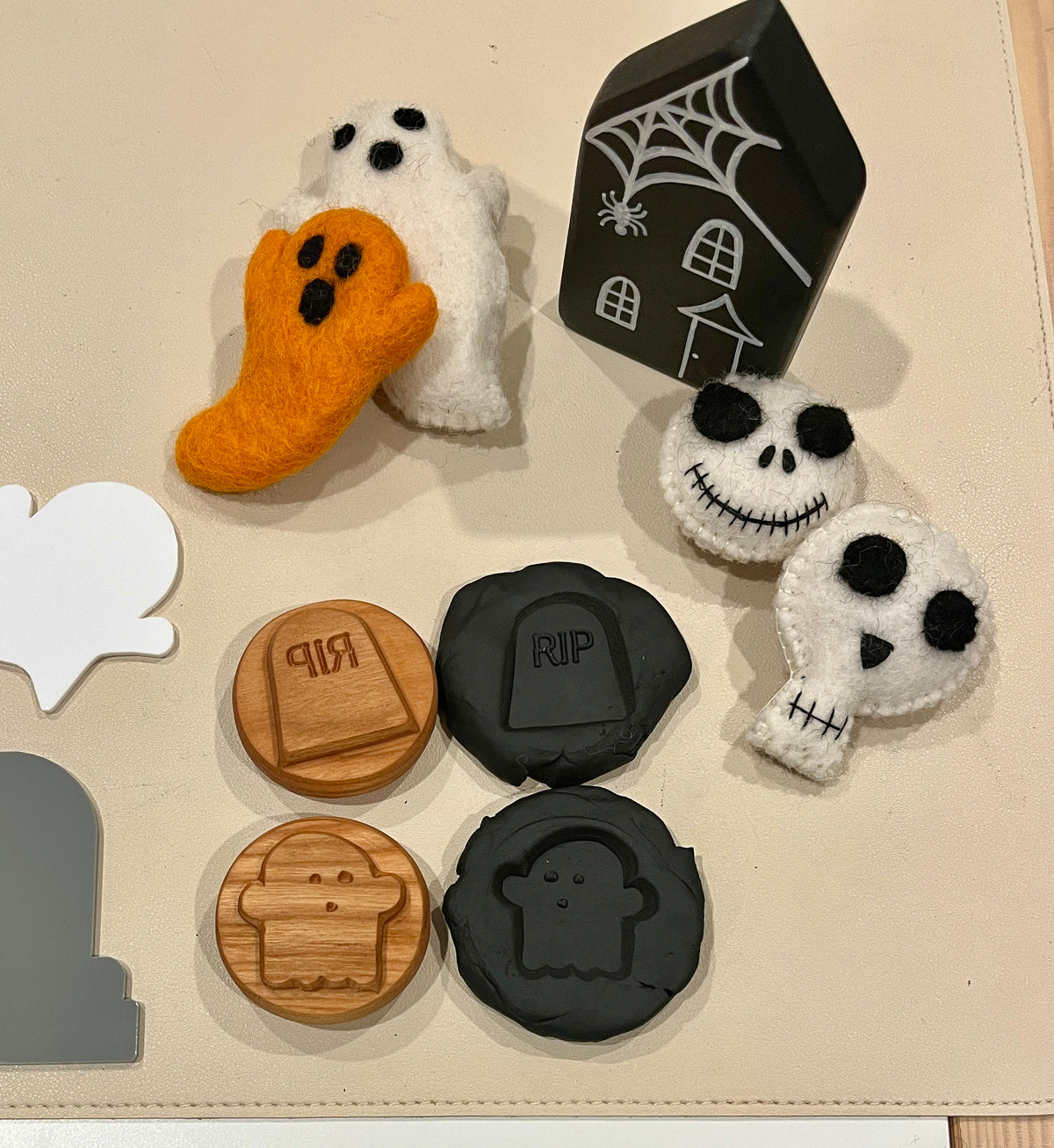 Felt ghost and skull figures with stitched eyes, wooden and black tokens engraved with ghost and RIP tombstone designs, and a black house with a spiderweb detail