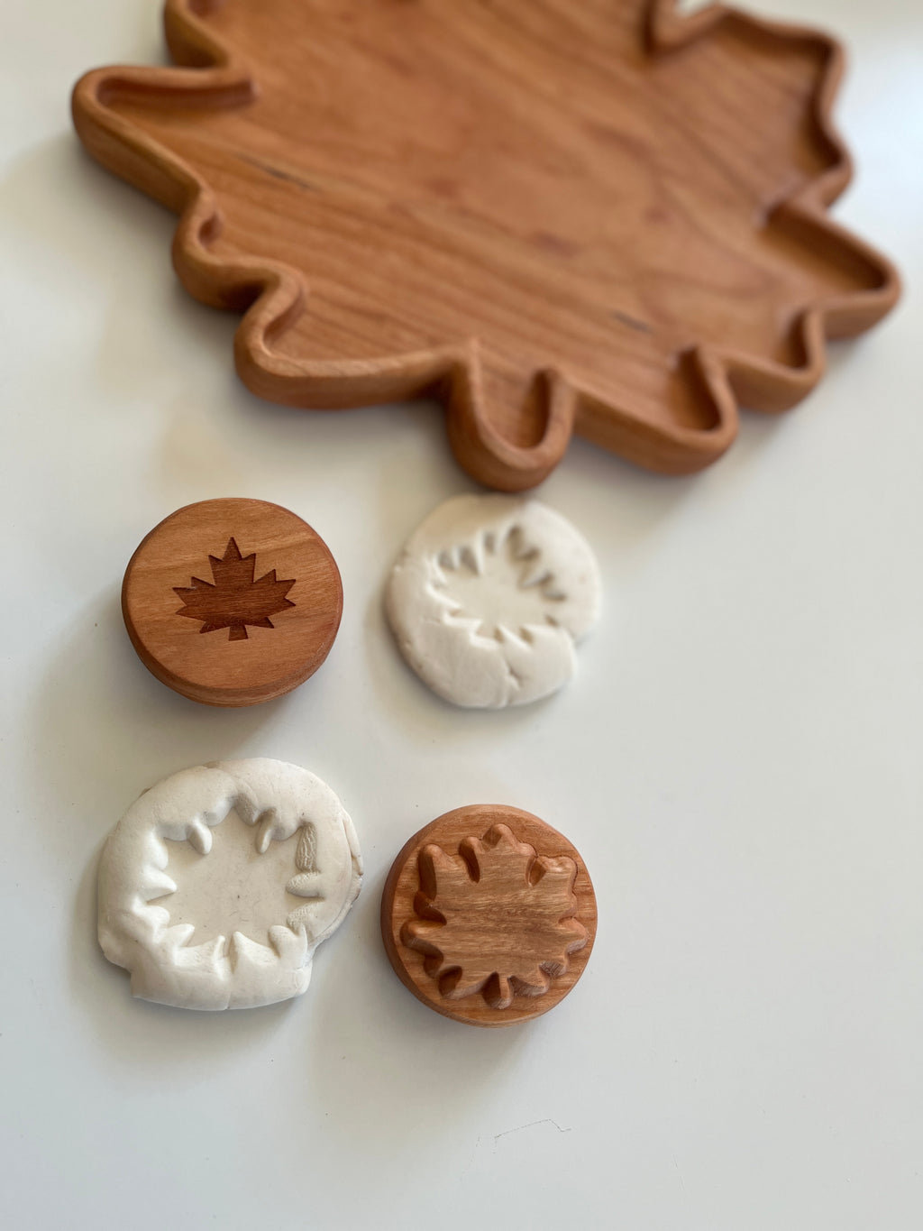 Wooden leaf-shaped tray with two wooden leaf stamps and white clay impressions on a white surface.