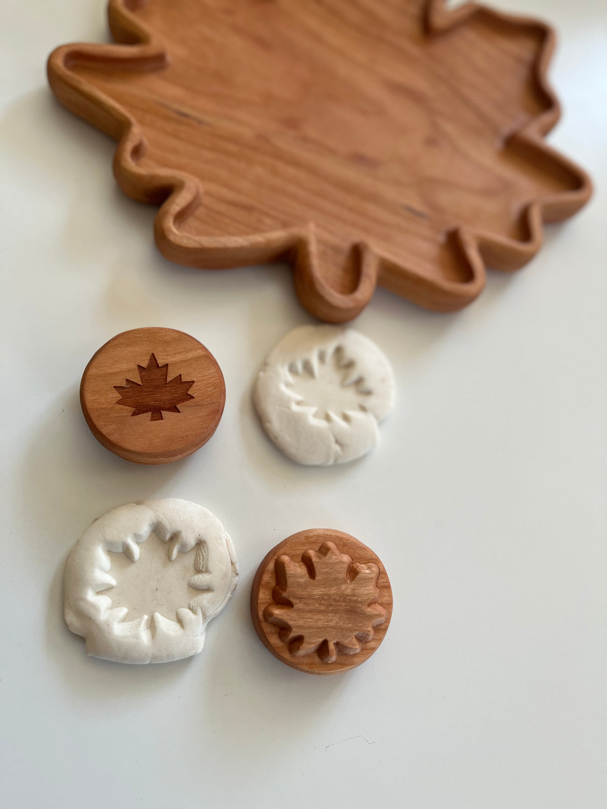 Wooden leaf-shaped tray with two wooden leaf stamps and white clay impressions on a white surface.