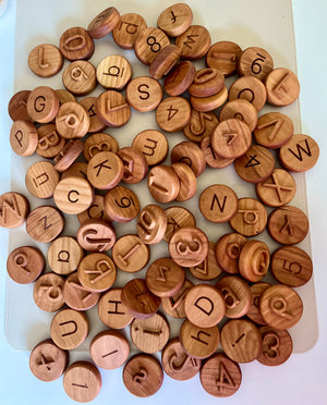 Assorted round wooden tokens engraved with uppercase letters and numbers scattered on a white surface