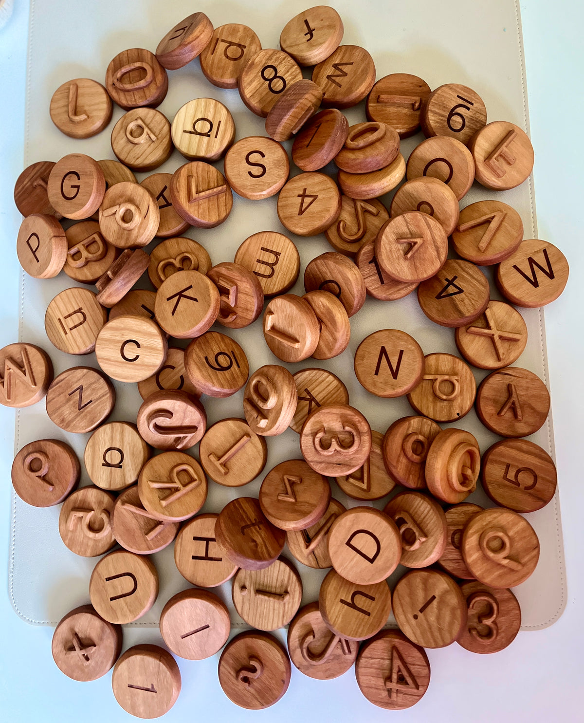 Assorted round wooden tokens engraved with uppercase letters and numbers scattered on a white surface