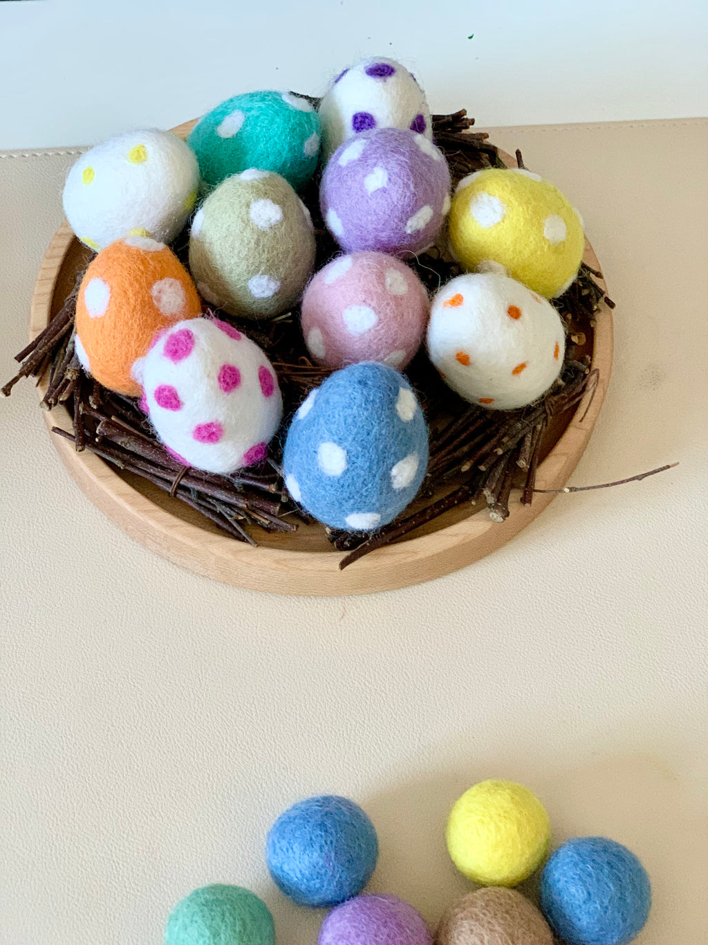 Nest of twigs holding colorful felt eggs with white, pink, and orange polka dots on a wooden base