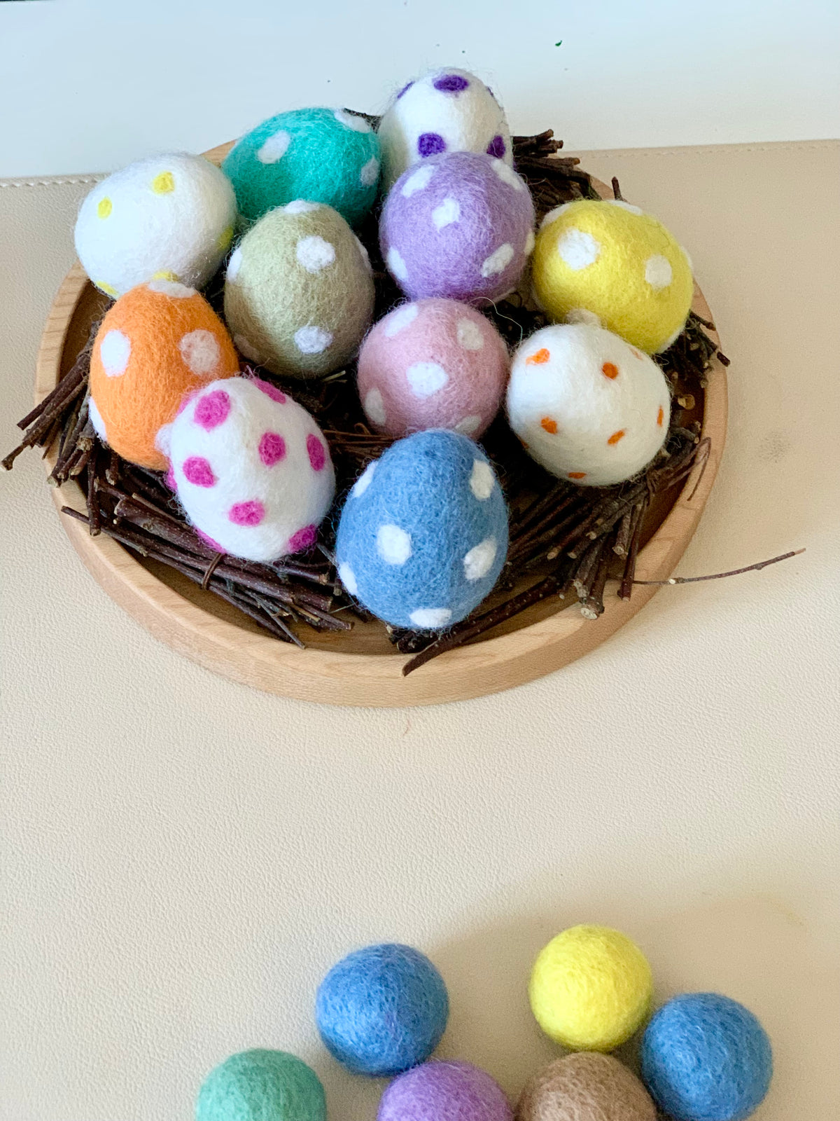 Nest of twigs holding colorful felt eggs with white, pink, and orange polka dots on a wooden base