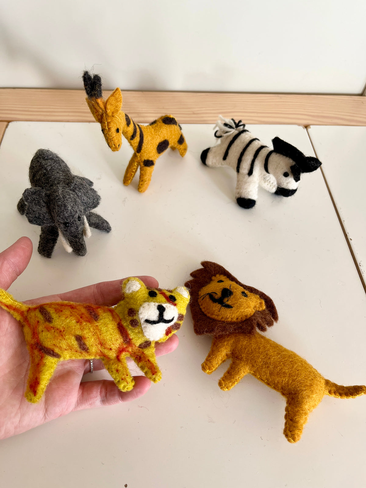 Handmade felt animal toys including a tiger, lion, elephant, giraffe, and zebra on a white surface