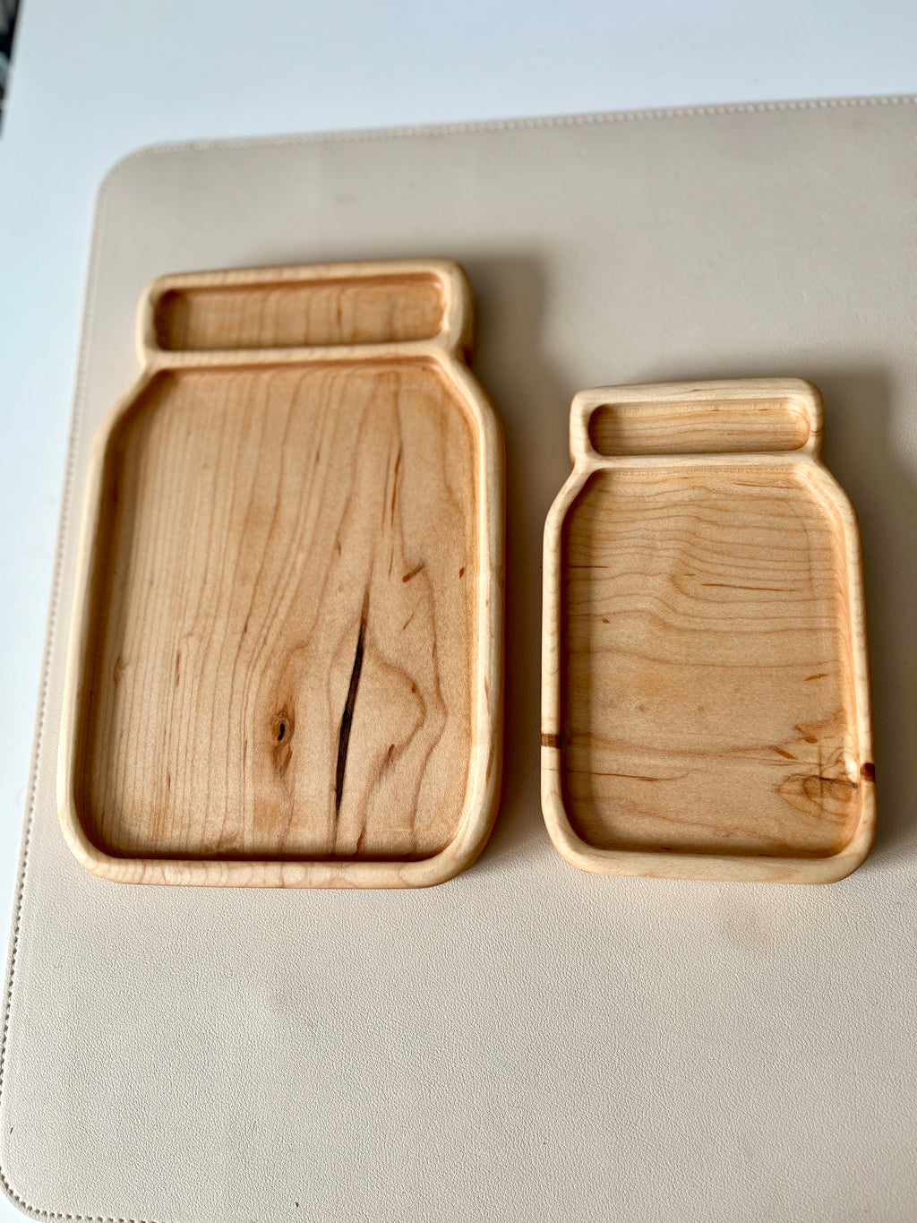 Two wooden trays shaped like jars with natural wood grain on a light surface background