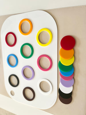 White board with colorful plastic rings in rows and matching solid discs stacked beside it on a beige surface