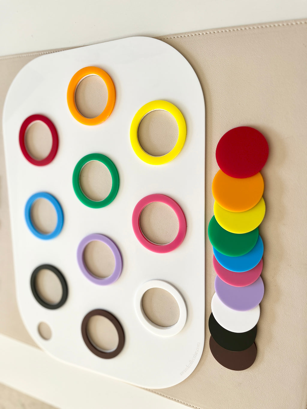 White board with colorful plastic rings in rows and matching solid discs stacked beside it on a beige surface