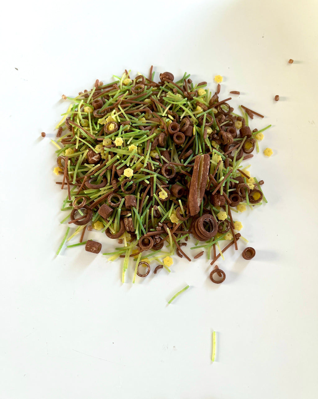 Small pile of brown and green thin noodle-like pieces mixed with tiny yellow star-shaped bits on white surface