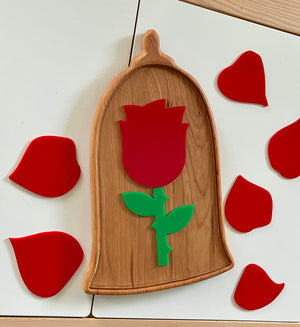 Wooden tray shaped like a bell with a red rose and green stem inside, surrounded by scattered red petal shapes on a white surface