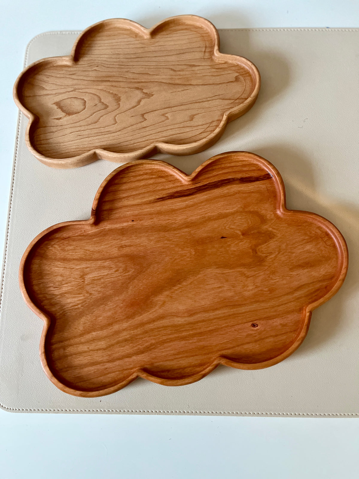 Two cloud-shaped wooden trays with different wood tones placed on a light textured surface