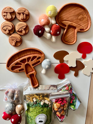 Wooden mushroom-shaped trays and tokens with felt mushroom toys, colorful pasta, and acrylic mushroom shapes on white surface