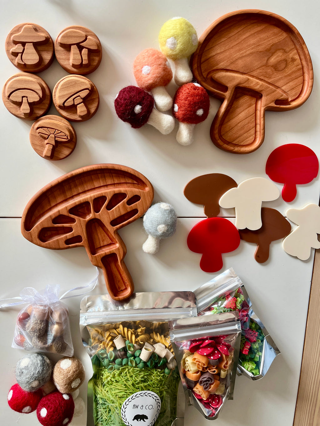 Wooden mushroom-shaped trays and tokens with felt mushroom toys, colorful pasta, and acrylic mushroom shapes on white surface