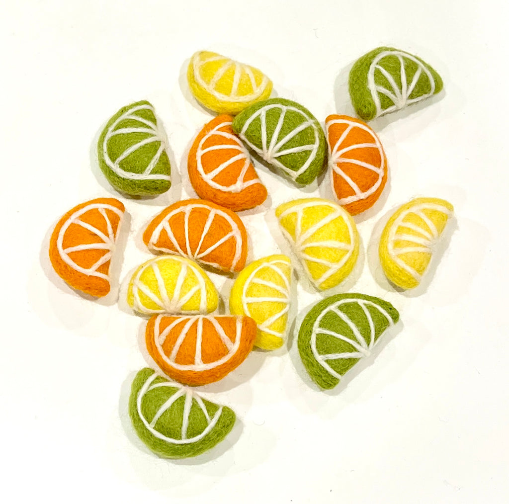 Felted wool pieces shaped like citrus fruit slices in green, yellow, and orange with white segment details on white background