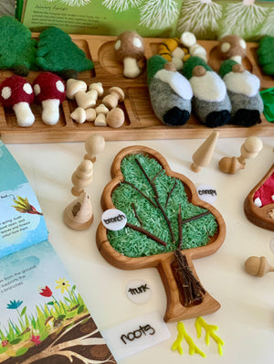 Tree-shaped wooden sensory tray filled with green rice, small wooden figures, felt mushrooms, and gnome toys on white table