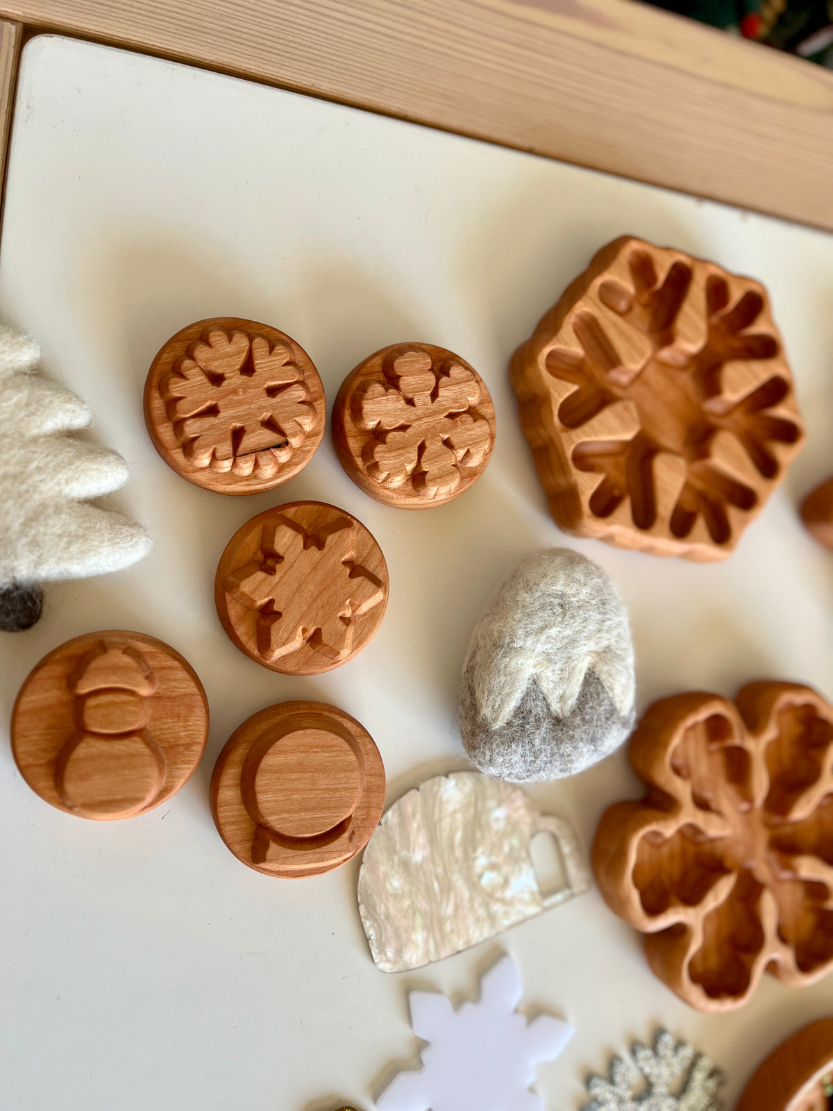 Wooden circular stamps with winter designs including snowflakes and a snowman on a white surface with felt decorations nearby