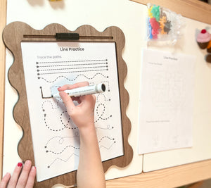 Child tracing lines on a worksheet with a wooden tray with dry erase insert.