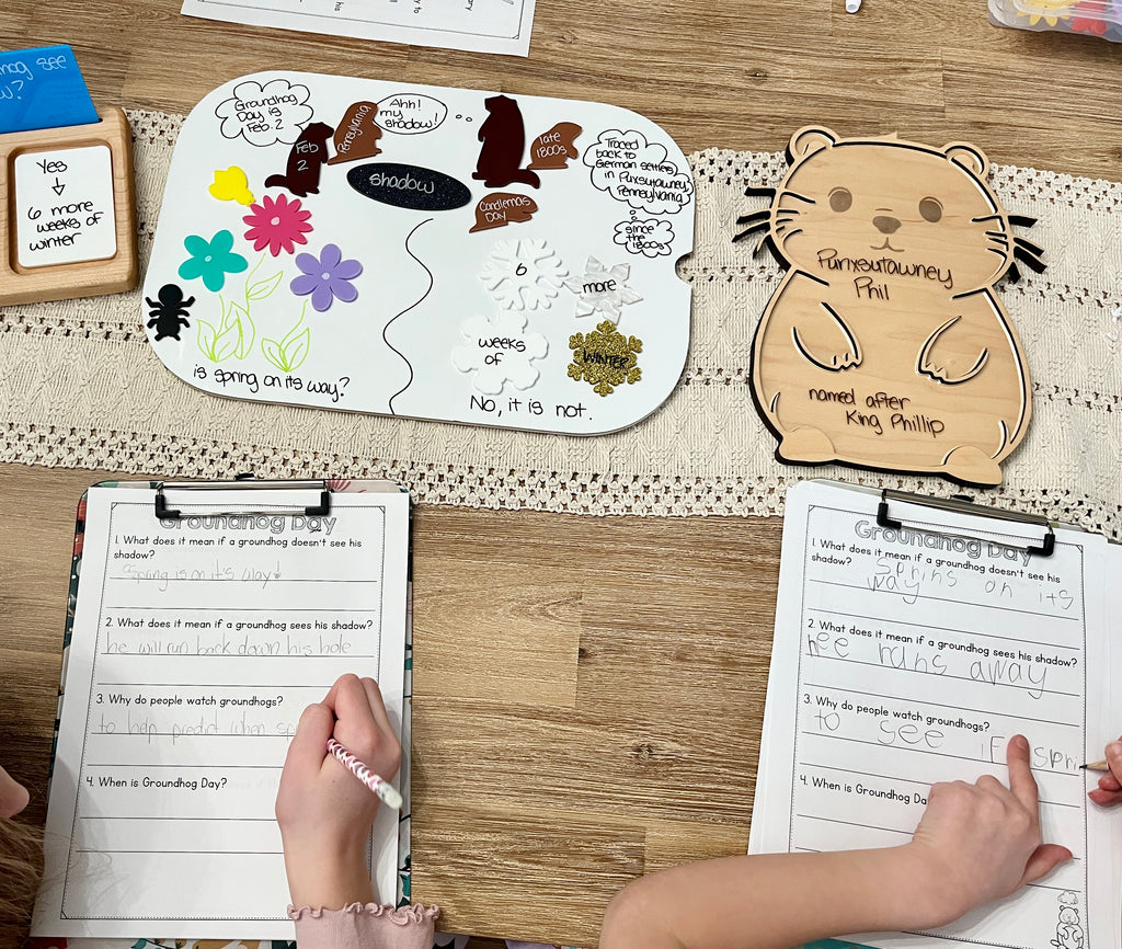 Laser Cut Groundhog Tray with Dry Erase Insert showing a wooden groundhog shape with educational notes, surrounded by handwritten worksheets and children's hands, handcrafted homeschool education resources.