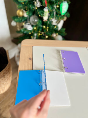 Person flipping through blue and white pages of small ring binder on wooden table near decorated Christmas tree