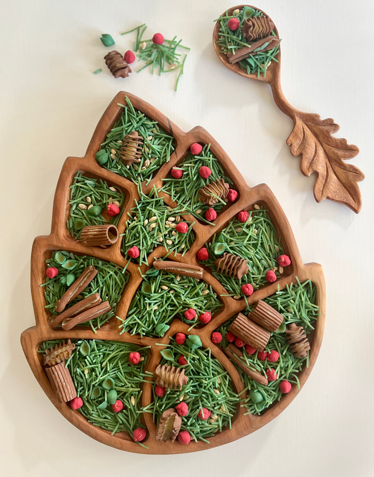 Wooden leaf-shaped serving tray with green herbs, red berries, cinnamon sticks, and a matching wooden serving spoon with leaf handle