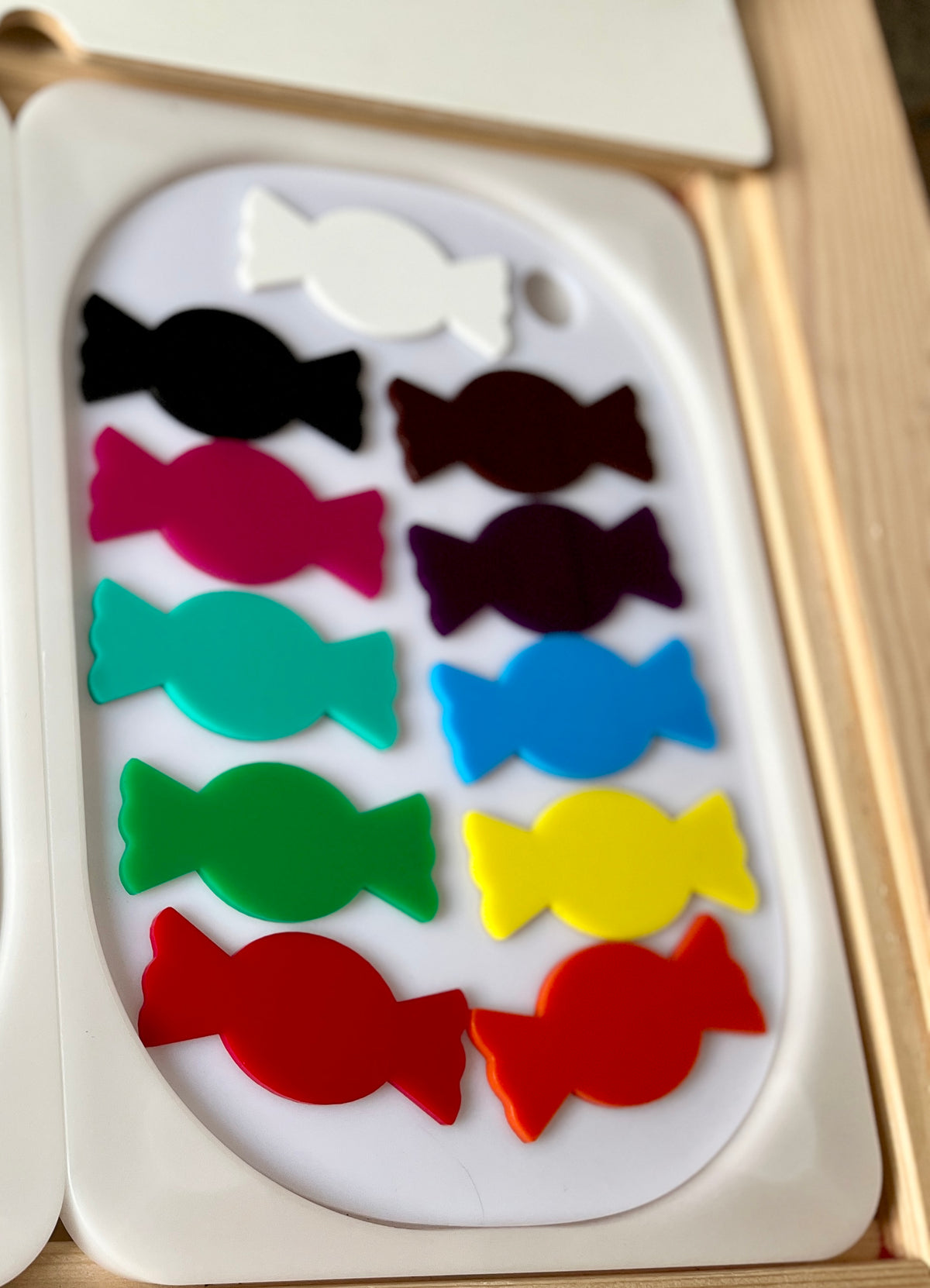 Ten candy-shaped cutouts in various colors arranged in two vertical columns on a white tray