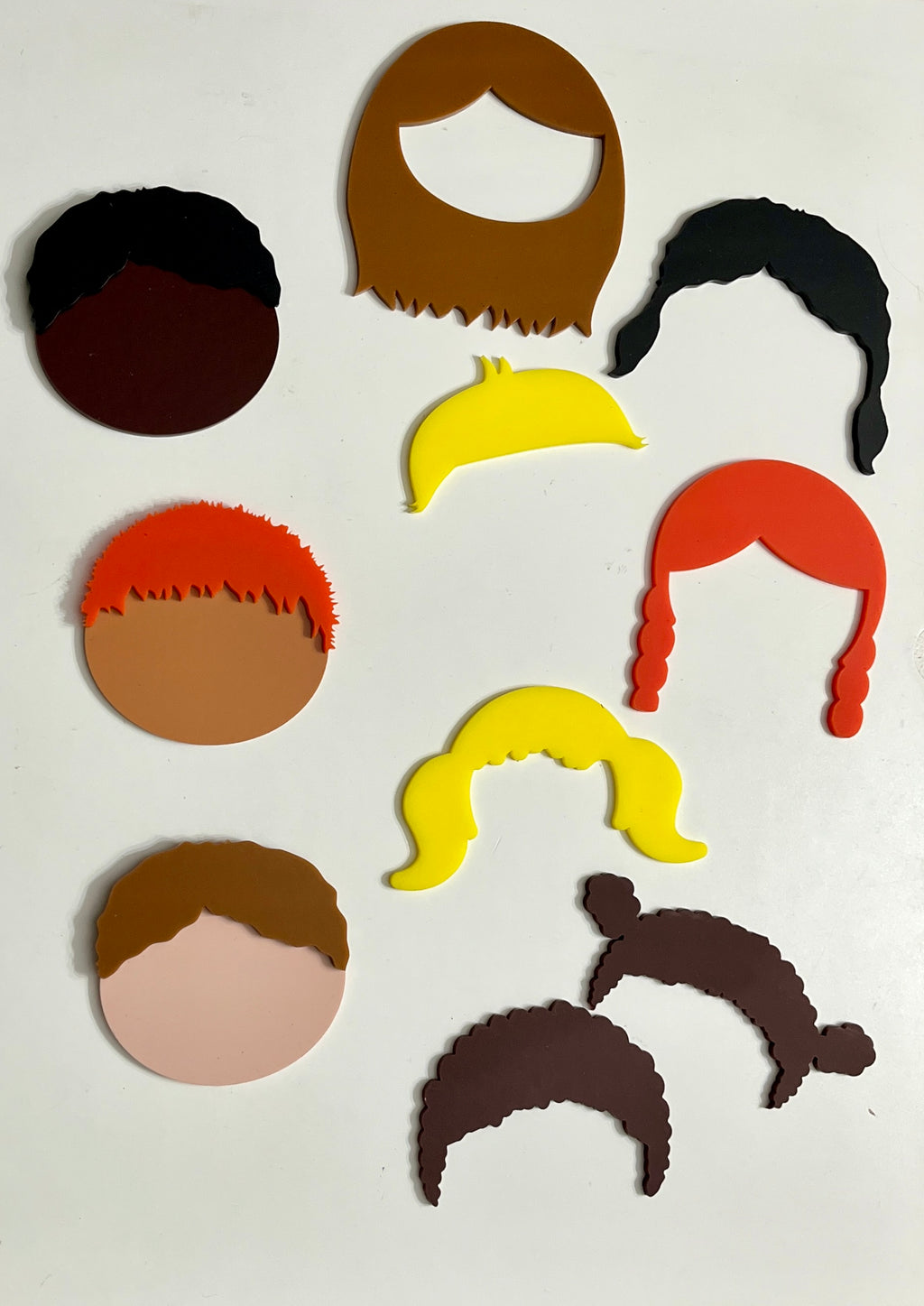 Assorted colorful flat face and hair cutouts in various styles and skin tones arranged on a white background