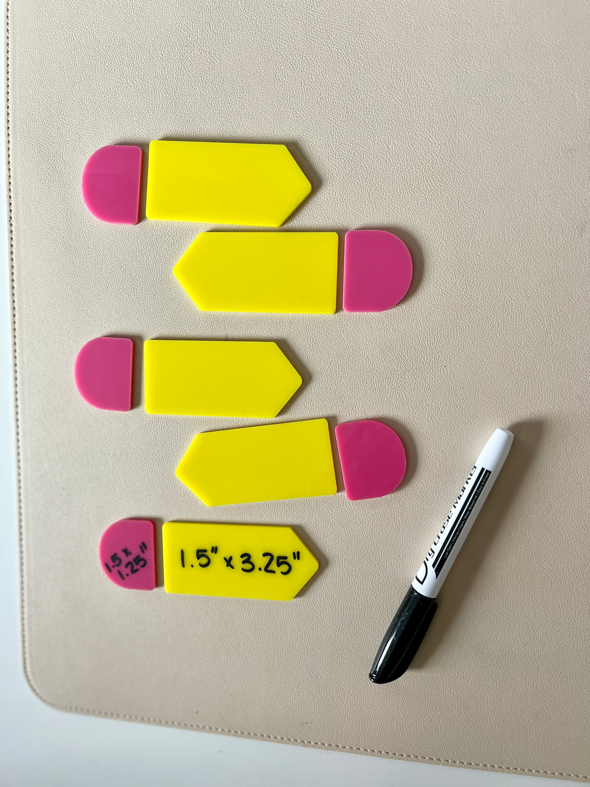 Five yellow plastic arrow-shaped tags with pink rounded ends and black marker pen on beige surface