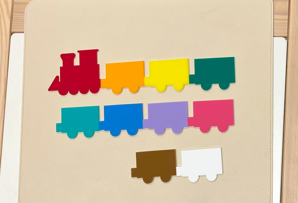 Colorful flat wooden train shapes in red, orange, yellow, green, teal, blue, purple, pink, brown, and white on a light background