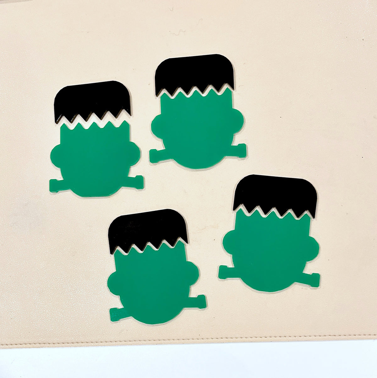 Four flat green Frankenstein head shapes with black zigzag hair on a light beige surface