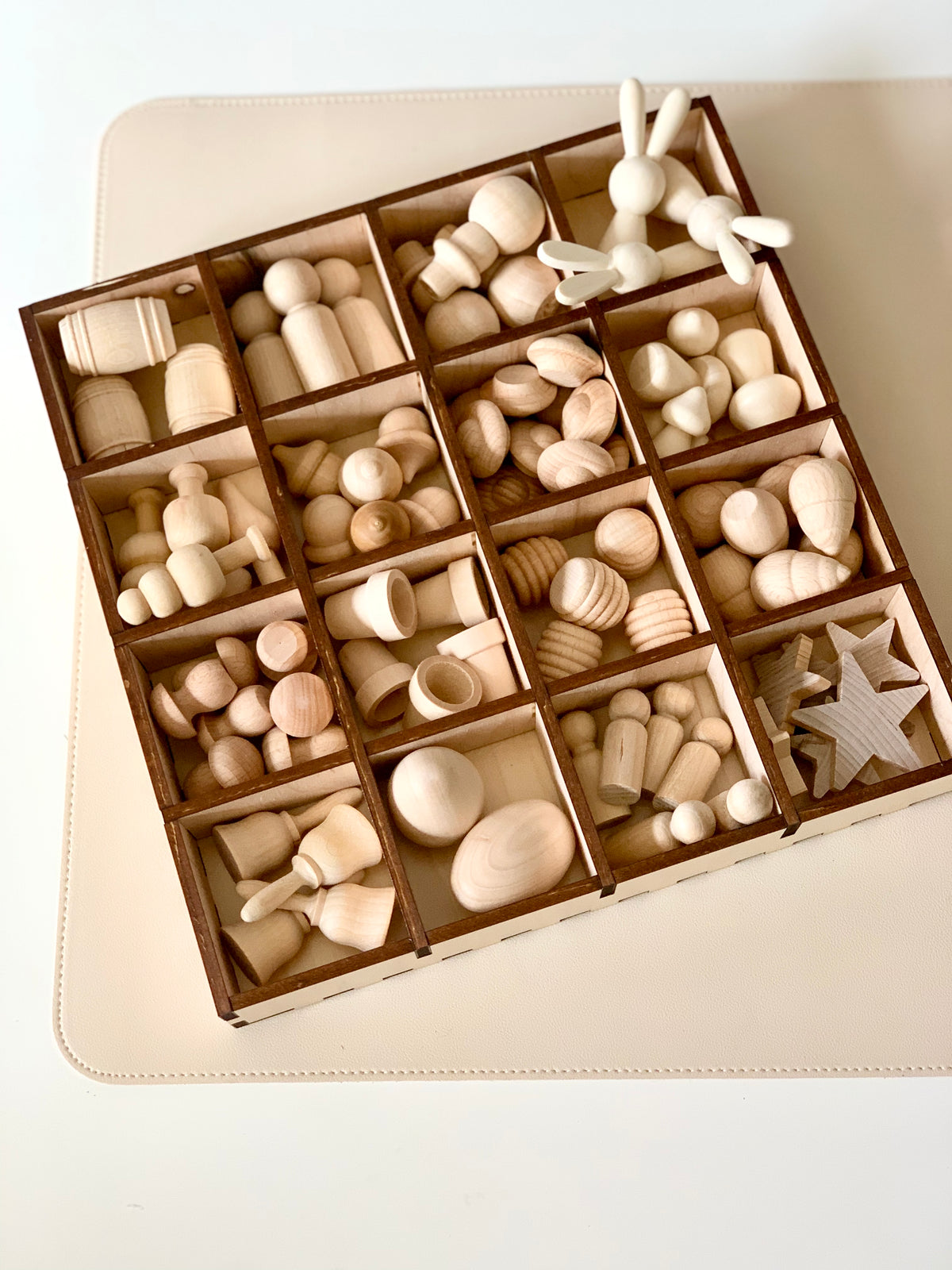 Compartmentalized wooden tray containing various unfinished wooden shapes including animals, spools, stars, and abstract figures
