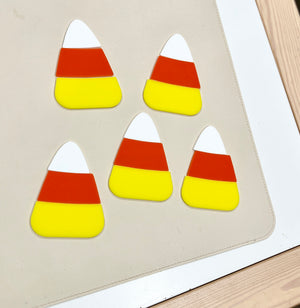 Five candy corn shaped pieces in white, orange, and yellow arranged on a cream-colored surface