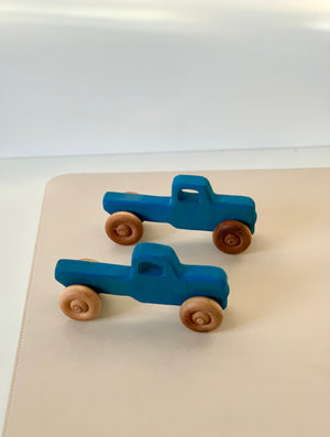 Two small blue wooden toy pickup trucks with natural wooden wheels on a beige surface