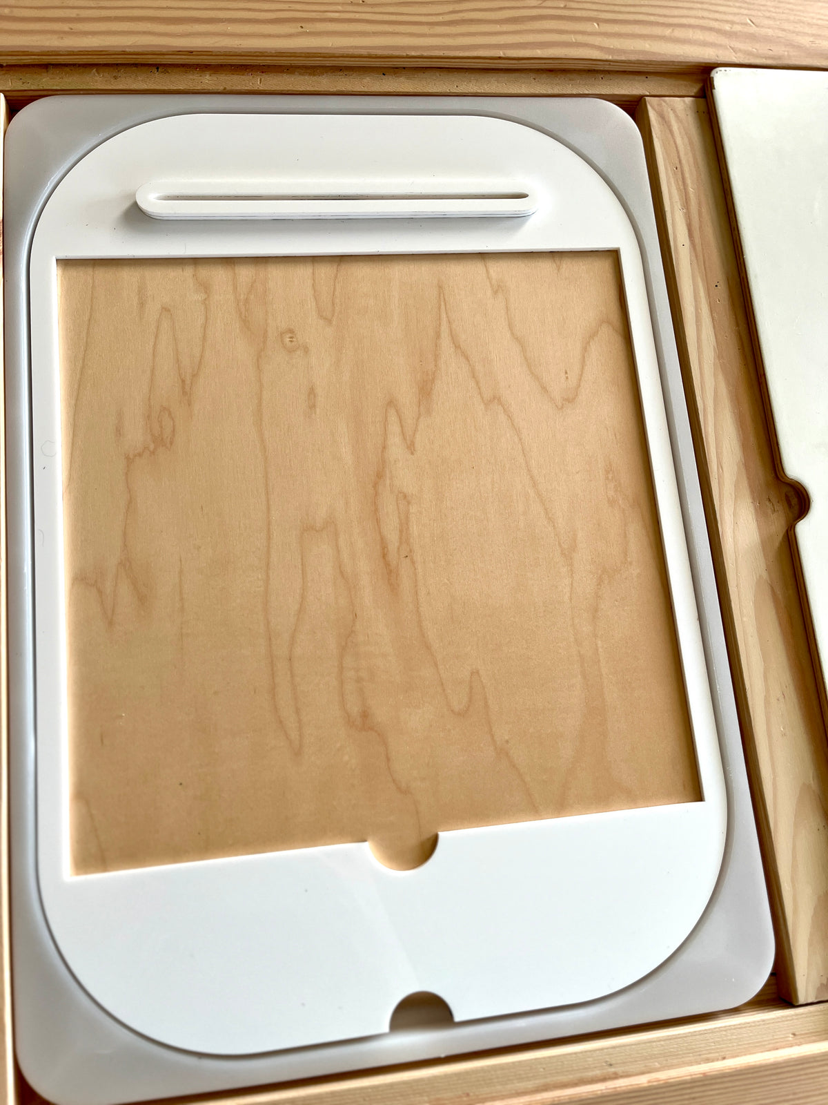 White plastic frame with rounded edges resting inside a wooden box on a wooden surface