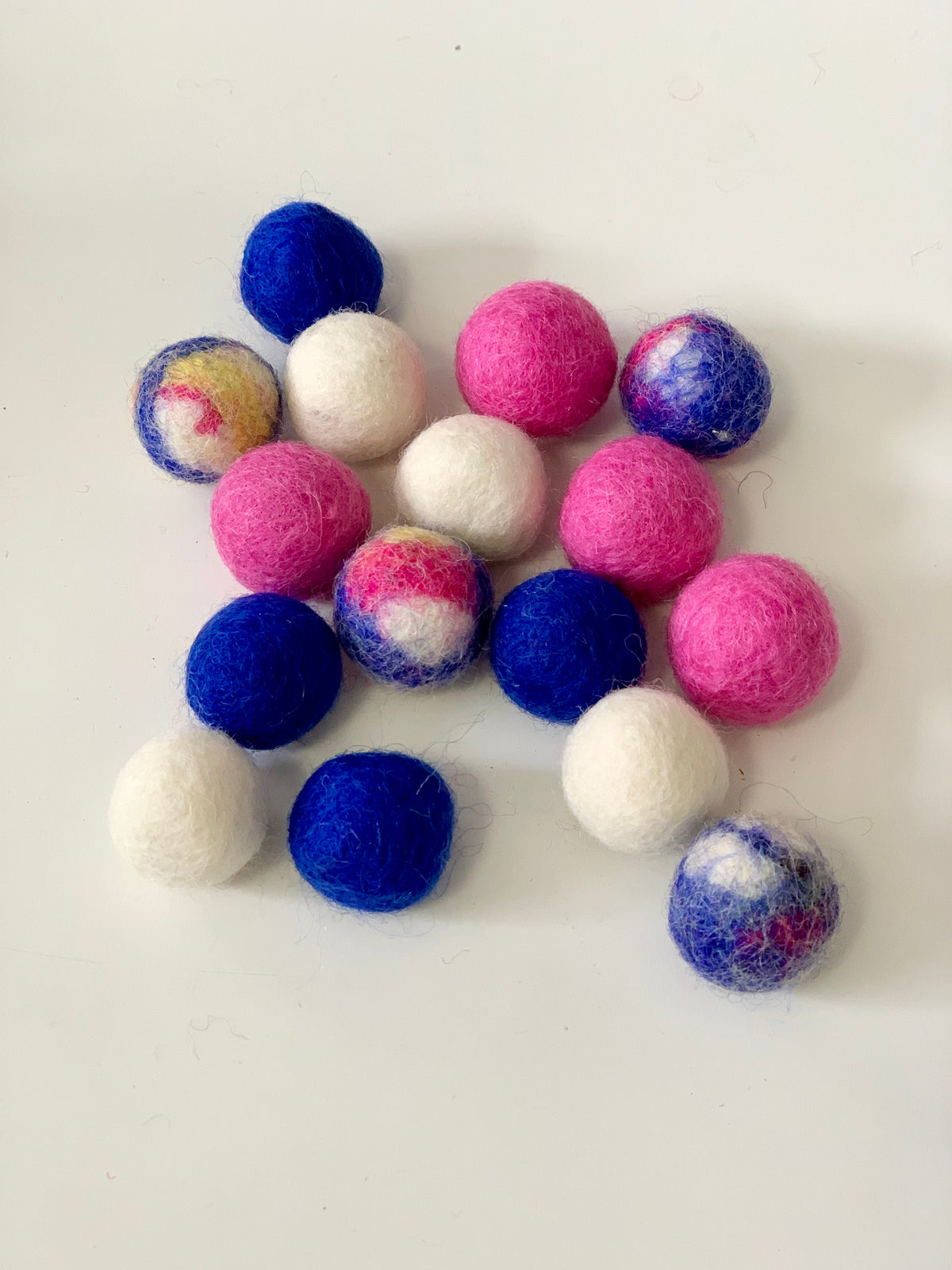 Assortment of small felt balls in blue, pink, white, and tye dye colors on white background