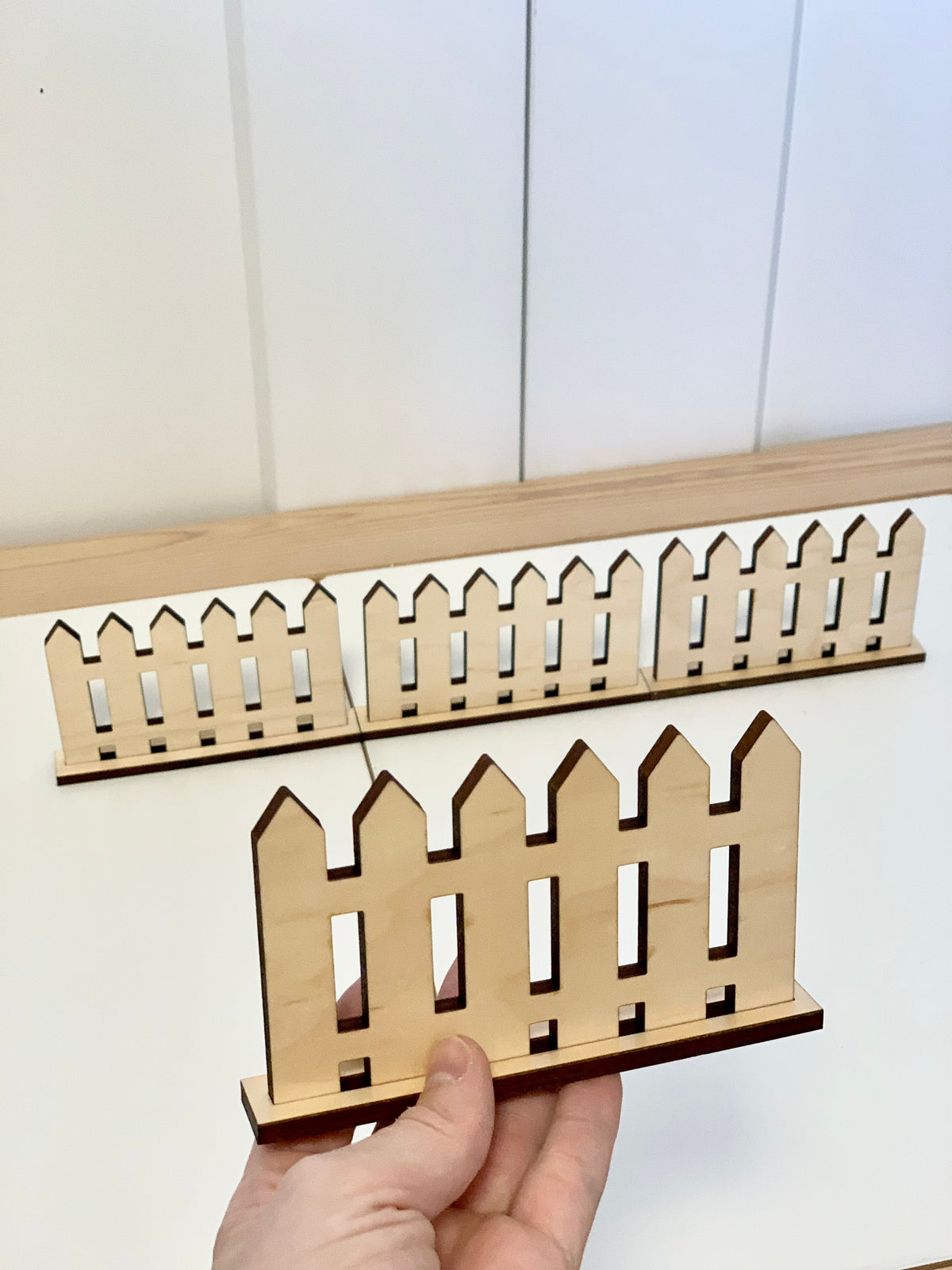 Small wooden play fences with freestanding bases arranged on white surface with hand holding one fence piece