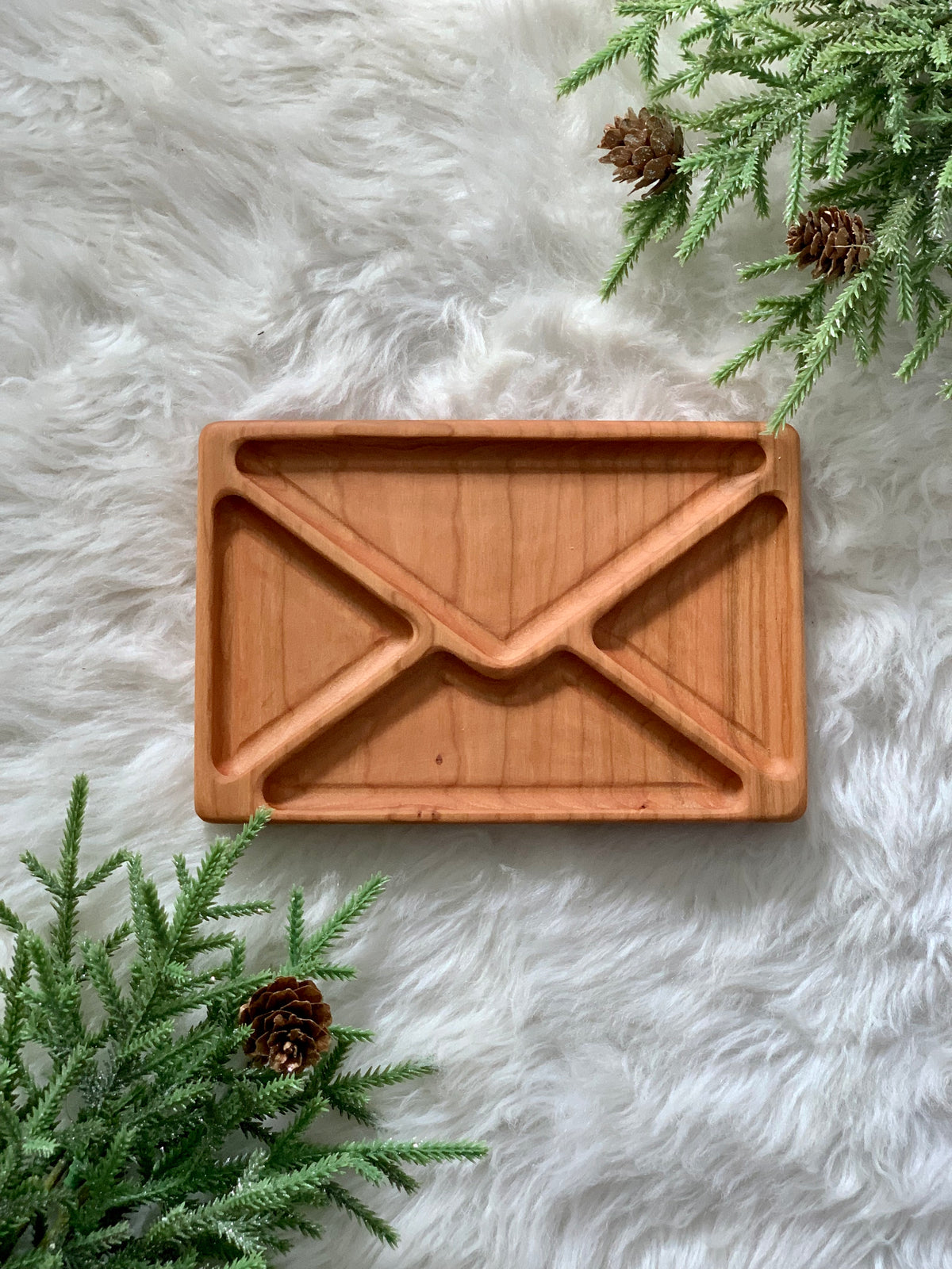 Wooden sensory tray shaped like an envelope displayed on white fur with pine branches and cones nearby