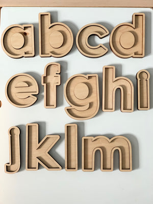 Laser cut wooden lowercase alphabet sensory trays arranged on white surface in three rows from a to m