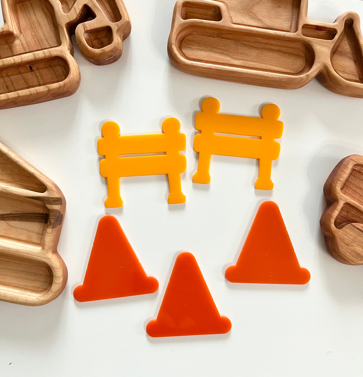 Wooden trays shaped like construction vehicles with orange traffic cones and yellow barrier tokens on white surface