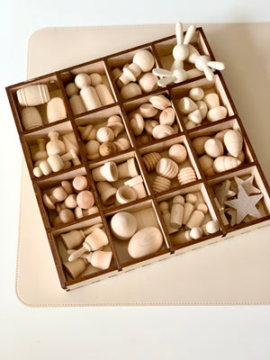 Wooden tray with multiple compartments holding assorted smooth unfinished wooden shapes including figures and geometric forms